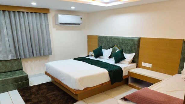 A hotel room with a large bed, bedside tables, a green sofa, and a window with curtains. - Hotel just inn (Ahmedabad)