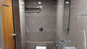 A modern bathroom with a marble floor, a wooden door, a glass shower enclosure, a toilet, and a sink. - Hotel just inn (Ahmedabad)