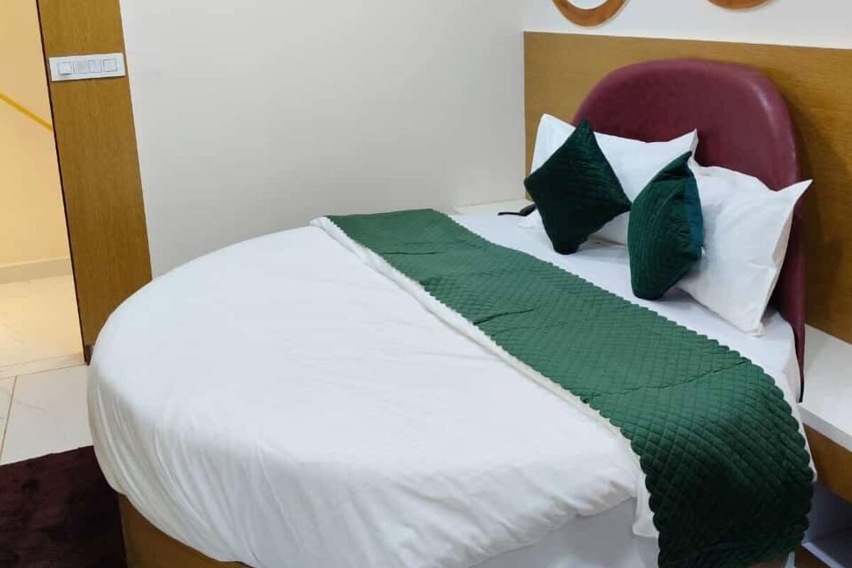 A modern bedroom with a round bed, white bedding, green throw, and a wooden headboard.