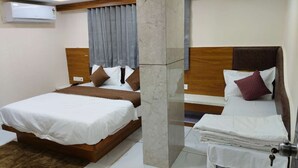 A hotel room with two beds, a marble pillar, a wooden headboard, and a grey curtain. - Hotel just inn (Ahmedabad)