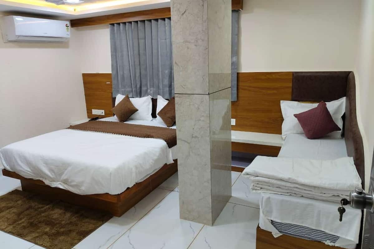 A hotel room with two beds, a marble pillar, a wooden headboard, and a grey curtain.