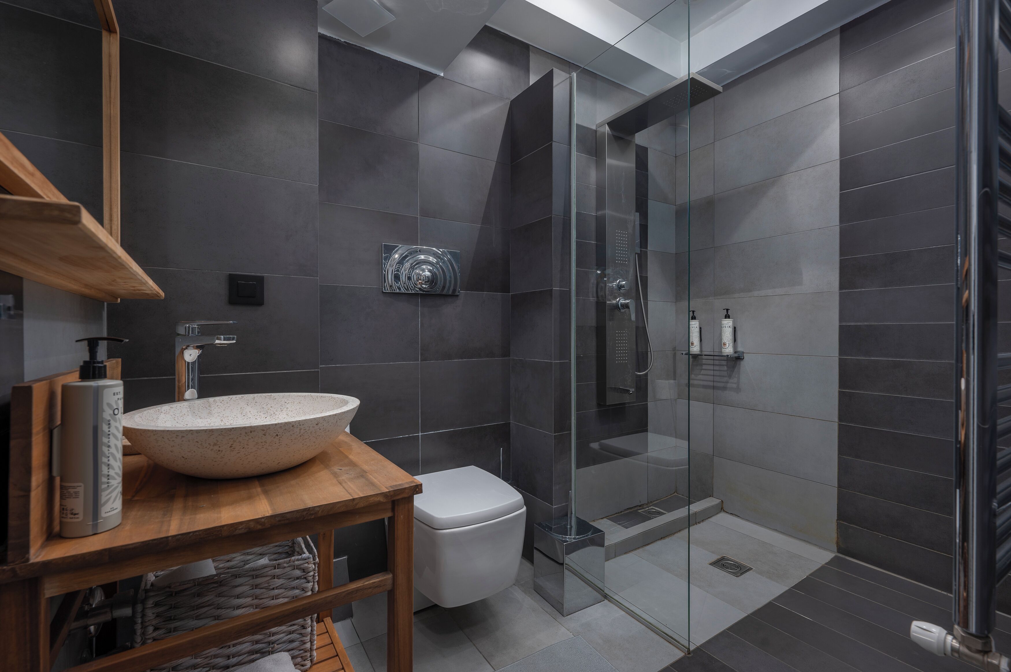 Een moderne badkamer met een groot wastafelobject, toilet, een douche met glazen wanden en een houten wastafelmeubel.