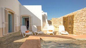 Un área de piscina con sillas reclinables blancas y una pared de piedra.