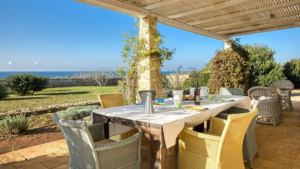 Un área de comedor al aire libre con sillas de mimbre y una mesa preparada para dos, con vista a un paisaje marino.