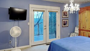 Un dormitorio con una cama, un televisor montado en la pared, una araña y un ventanal corredero que da a un balcón.