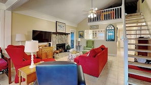Una sala de estar con chimenea, sofás rojos, un sillón azul y una escalera.