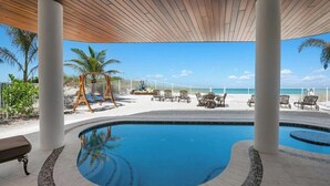 A pool area with a wooden ceiling, white columns, and a view of the beach.