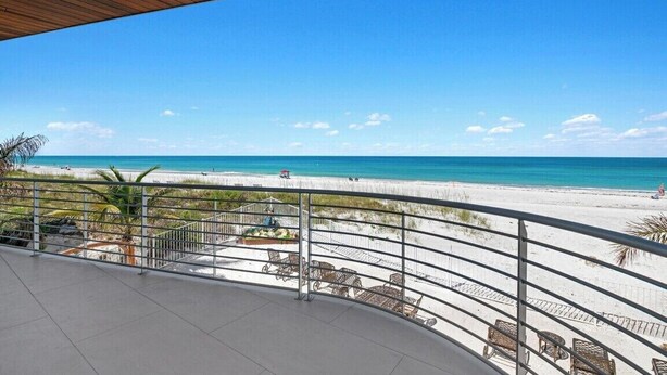A balcony with a view of a beach, featuring a railing, chairs, and a wooden ceiling.