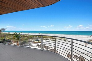 Un balcon donnant sur une plage, avec une balustrade, des chaises et un plafond en bois.