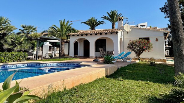 A poolside area with a clear blue sky, palm trees, and a white building with arches. - LA CASITA | ideal villa for small families | 2 double bedrooms | private pool (Teulada)