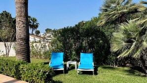 A garden with two blue lounge chairs, a palm tree, and a tiled patio area. - LA CASITA | ideal villa for small families | 2 double bedrooms | private pool (Teulada)