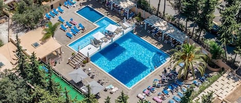 An aerial view of a resort with two swimming pools, lounge areas, and palm trees.