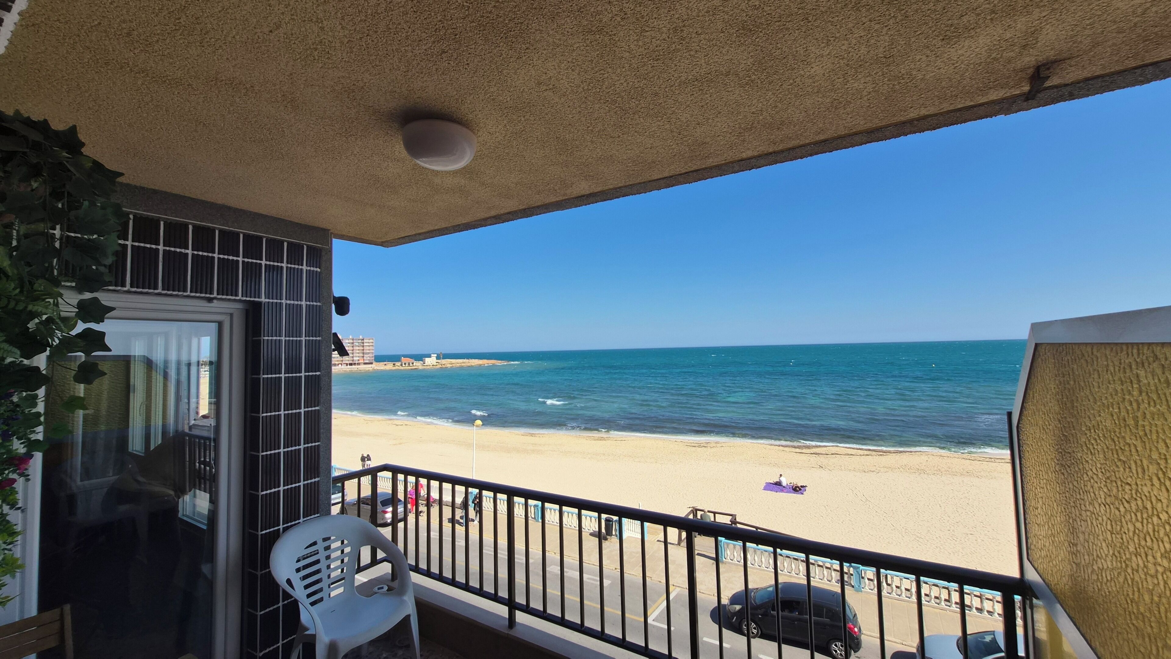 Un balcó amb vista a la platja, una cadira i una barana.