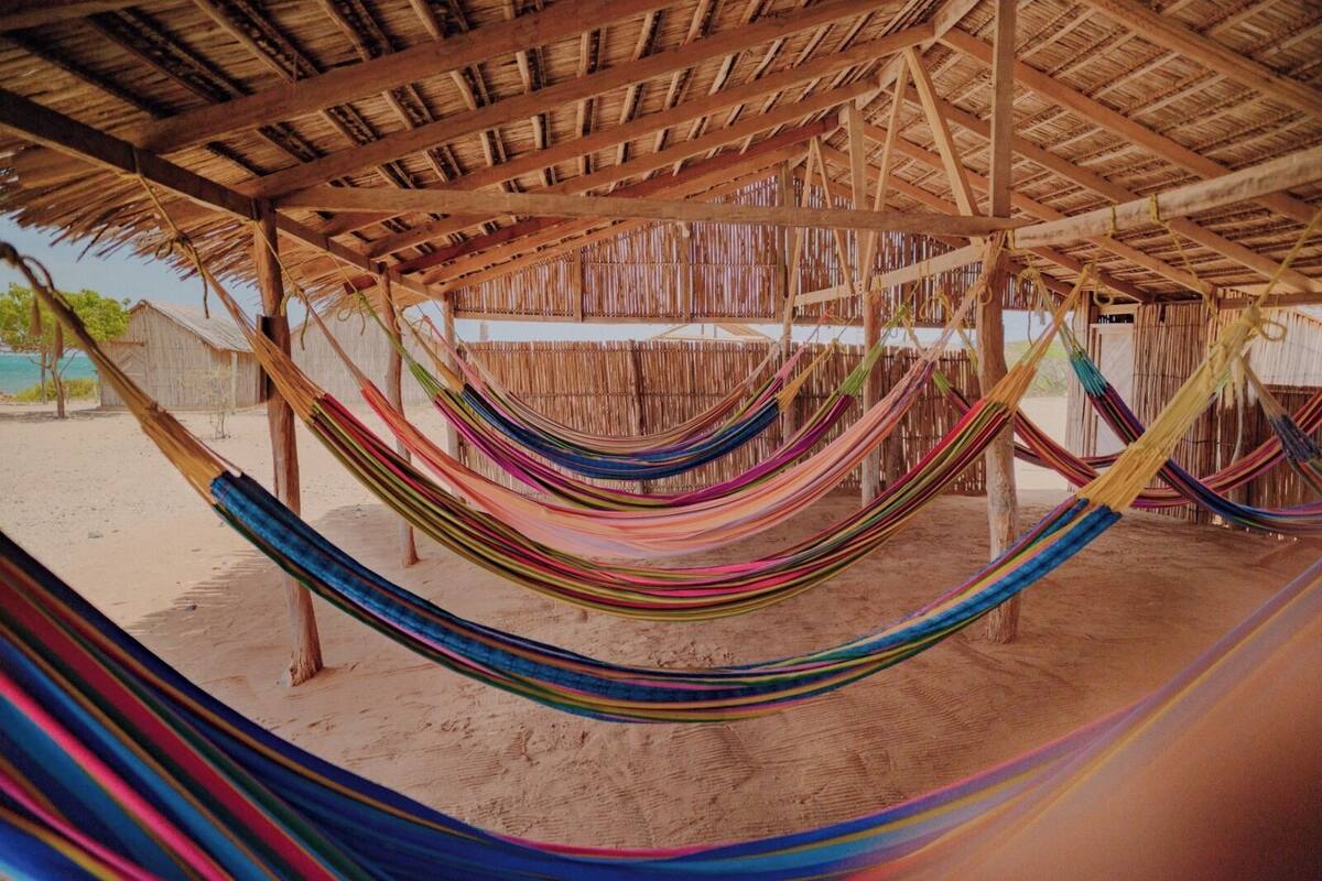 A beach with multiple colorful hammocks under a wooden structure.