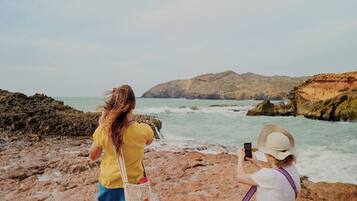 Two people on a rocky beach, one taking a photo, the other sitting and using a phone.