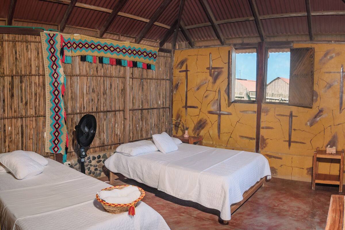 A room with two beds, a fan, and a rustic decor.