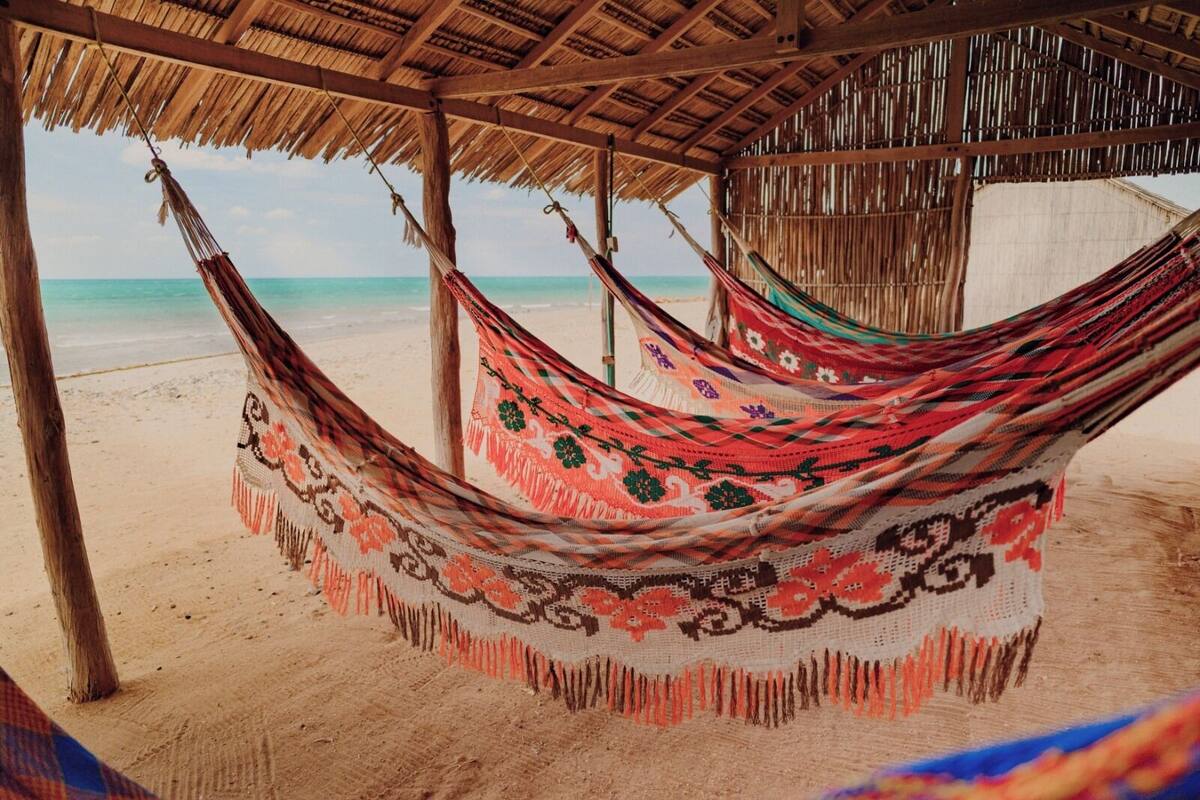 A hammock under a thatched roof structure on a sandy beach.