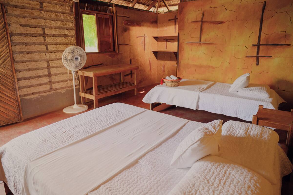 A room with two beds, a fan, a wooden desk, and a window.