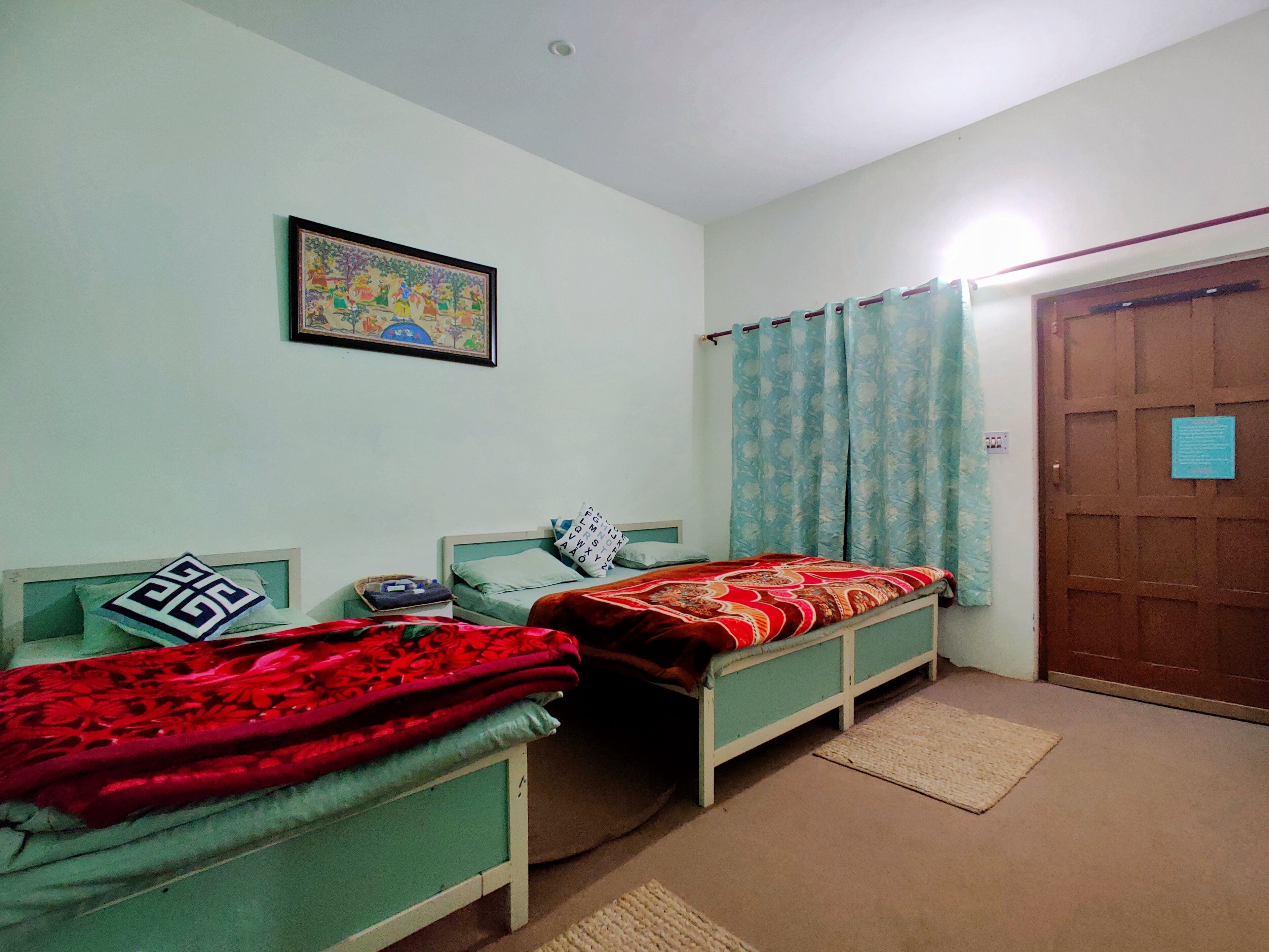 Ein Zimmer mit zwei Einzelbetten, einem gerahmten Bild an der Wand und einer Tür mit einem Schild.