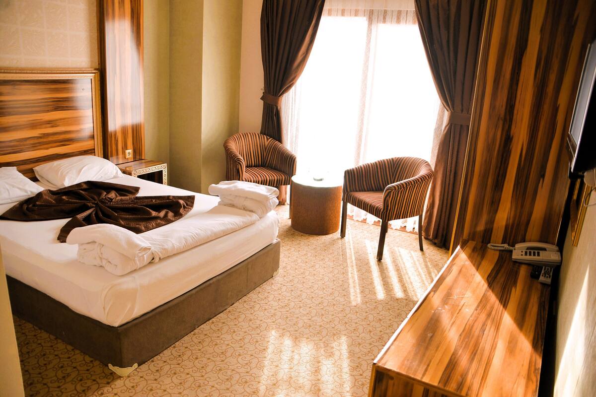 Une chambre d’hôtel avec un grand lit, deux fauteuils, une petite table et un téléphone sur la table de chevet.