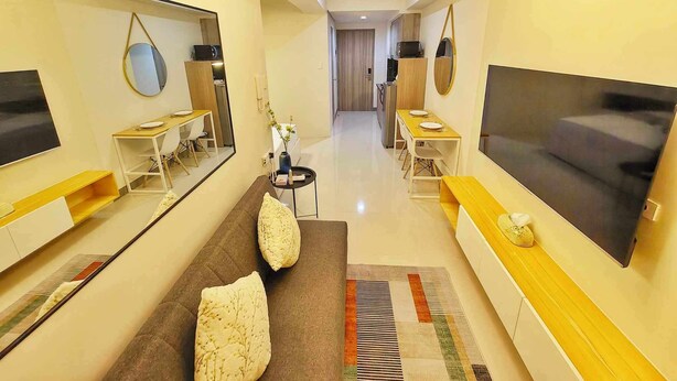 A modern hotel room with a large bed, a TV, a desk with a chair, a mirror, and a bathroom visible through an open door. - Homefort at S Residences (Pasay)
