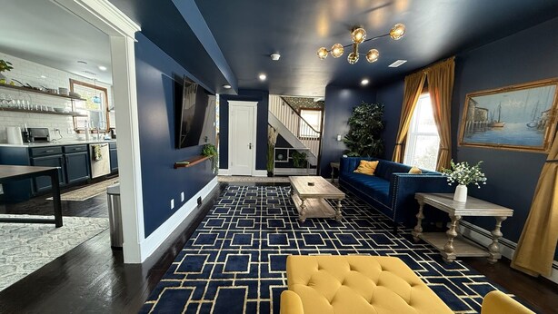 Un soggiorno moderno con una parete blu scuro, un divano giallo e un tappeto decorato.