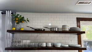 Una cucina con pareti piastrellate in bianco, scaffali in legno con utensili da cucina, una pianta in vaso e una finestra con vista.