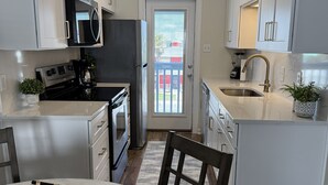 A modern kitchen with white cabinets, a black refrigerator, stainless steel appliances, and a dining area with a round table and chairs. - Newly Renovated Beachside Complex~2BR/1.5B w/Pool (Gulf Shores)