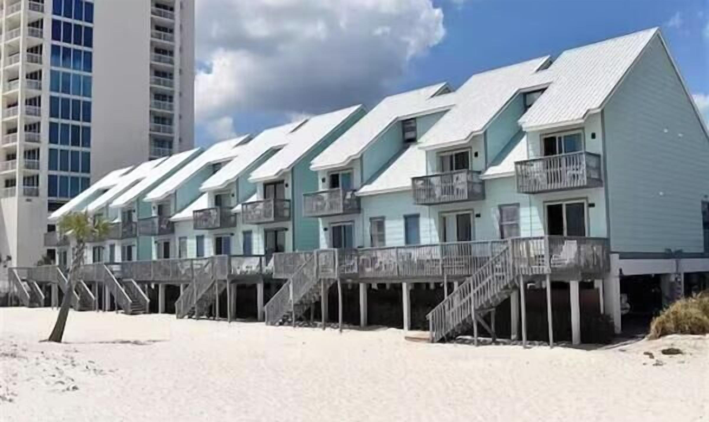 A beachfront hotel with multiple-story buildings, balconies, and a sandy beach area.