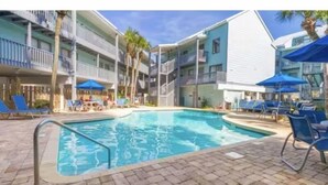A swimming pool with lounge chairs and umbrellas, surrounded by multi-story buildings with balconies. - Newly Renovated Beachside Complex~2BR/1.5B w/Pool (Gulf Shores)