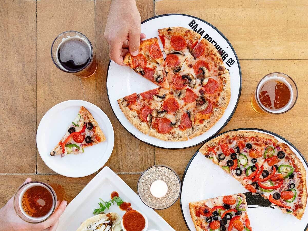 A wooden table with pizza slices, a glass of beer, and a plate of food.