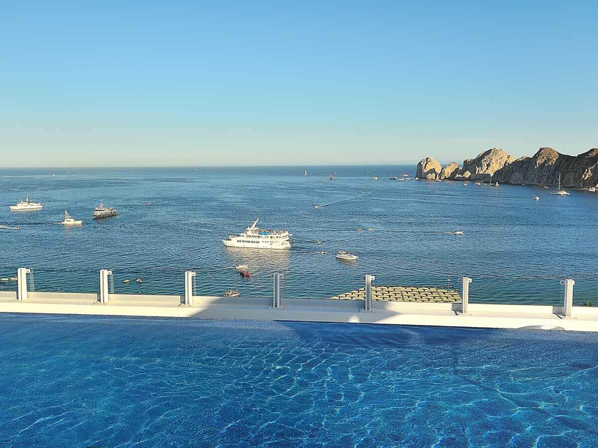 A pool with clear blue water, a rocky coastline, and several boats in the distance.