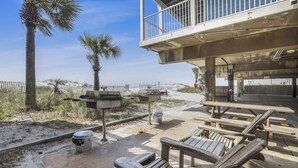 An outdoor seating area with wooden benches and picnic tables, a barbecue grill, and a trash can.