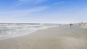 A beach with a clear sky, sandy shore, and a few people walking.
