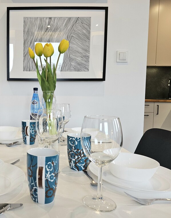 Una mesa de comedor dispuesta con tazas de diseño azul, un florero con flores amarillas y un cuadro abstracto enmarcado en la pared.
