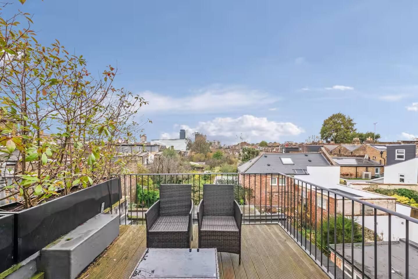 A rooftop terrace with two wicker chairs, a small table, and a view of the cityscape.