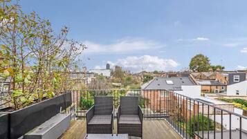 A rooftop terrace with two wicker chairs, a small table, and a view of the cityscape.
