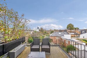 A rooftop terrace with two wicker chairs, a small table, and a view of the cityscape.