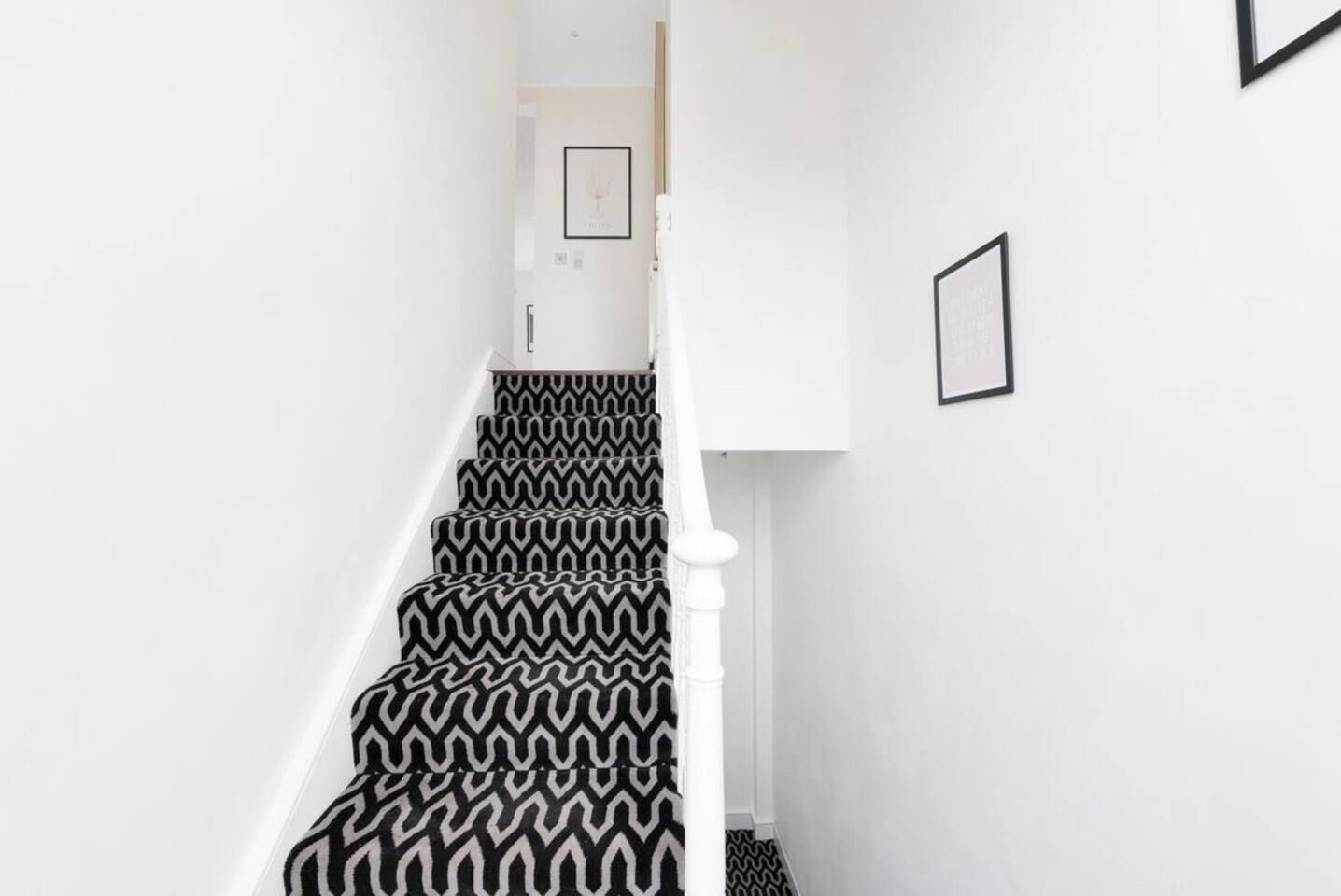 A staircase with a black and white zigzag patterned carpet, white walls, and a white railing.