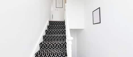 A staircase with a black and white zigzag patterned carpet, white walls, and a white railing.