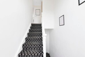 Un escalier avec un tapis à motifs zigzag noir et blanc, des murs blancs et une rampe blanche.