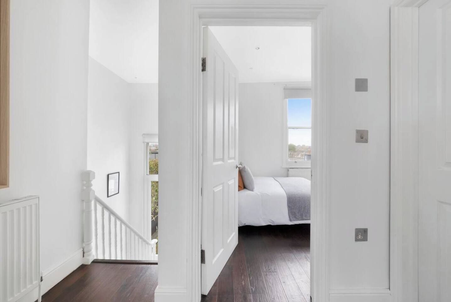 A hallway leading to a bedroom with a bed, a window, and a view of the outdoors.