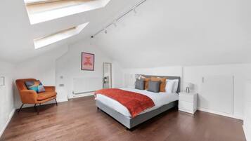 A bedroom with a skylight, a bed, a nightstand, a chair, and a radiator.