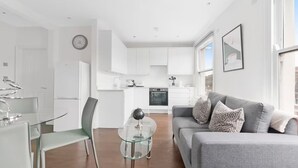Een moderne woonkamer met een grijze bank, een glazen salontafel en een eethoek met een glazen tafel en stoelen.