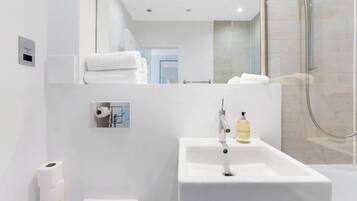 A modern bathroom with a white sink, a mirror, and a shower area.