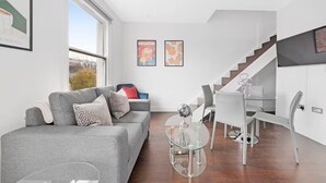 Een moderne woonkamer met een grijze bank, een glazen salontafel, en een eethoek met een glazen tafel en stoelen.