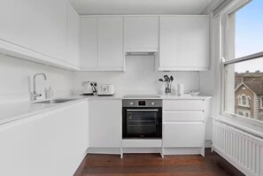 A compact kitchen with white cabinetry, a built-in oven, and a window offering a view of the outside.