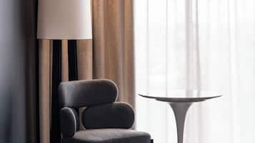 Una silla moderna y una mesita en una habitación con un ventanal, cortinas y una lámpara.