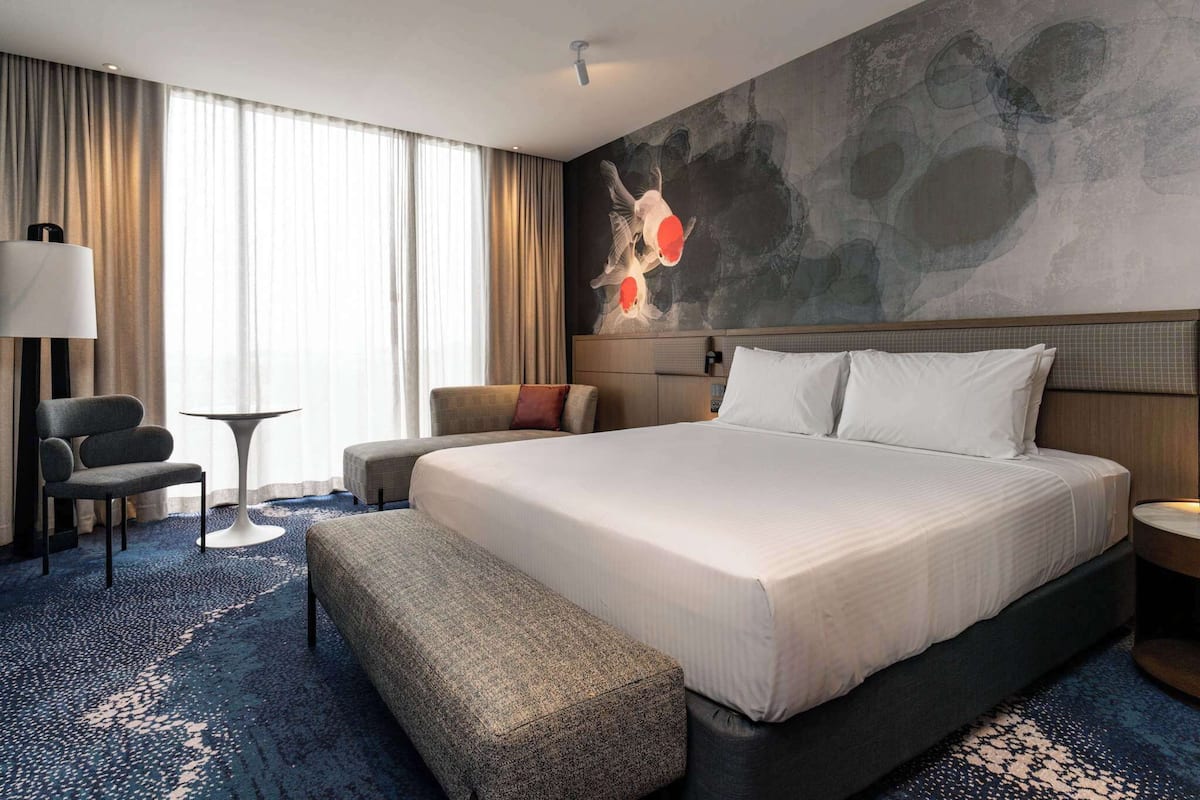 A hotel room with a large bed, a desk, a chair, and a small table.