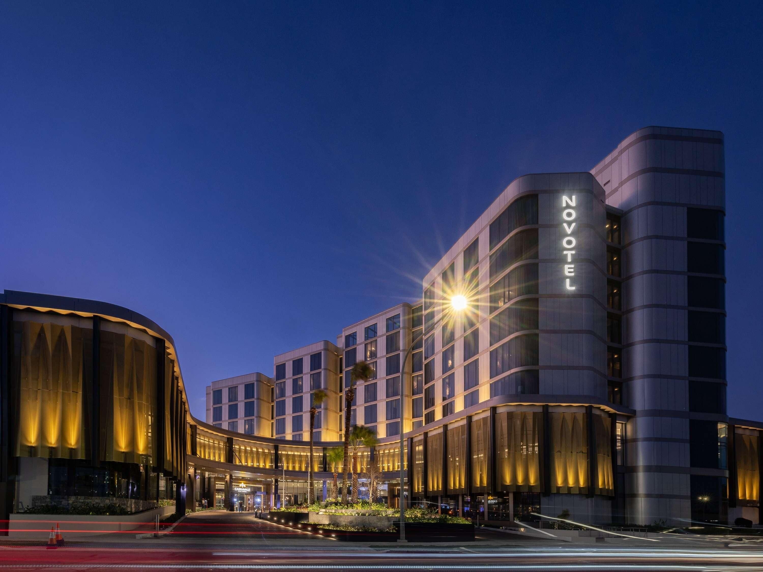 Un hotel moderno con un llamativo letrero de 'NOVOTEL', que presenta una fachada curva y una entrada bien iluminada.